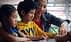 A woman assisting two children with drawing activities at a table. - Olive Oil Times