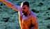 A shirtless man with a muscular build raising his arm in celebration outdoors. - Olive Oil Times