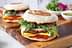 Breakfast sandwich featuring a fried egg, sausage patty, and fresh greens on a toasted bun. - Olive Oil Times