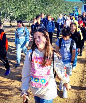 A group of students walking in an olive grove, wearing backpacks and casual clothing. - Olive Oil Times