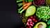An assortment of fresh vegetables including carrots, celery, and avocado arranged on a dark surface. - Olive Oil Times