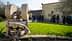 Old stone olive oil pressing equipment displayed outdoors near a building with visitors observing. - Olive Oil Times