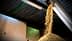 Grain cascading from a hopper onto a pile on the ground in a warehouse setting. - Olive Oil Times