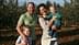 A family of four posing together in an olive grove, with two children and two adults smiling at the camera. - Olive Oil Times