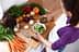 Individual pouring oil over a bowl of salad with various fresh vegetables on a wooden countertop. - Olive Oil Times