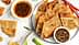 A plate of scallion pancakes arranged with two bowls of dipping sauces and green onions on a marble surface. - Olive Oil Times