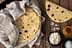 A stack of freshly made flatbreads wrapped in a cloth with flour and oil on a wooden surface. - Olive Oil Times