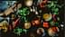 An overhead view of various cooking ingredients including vegetables, herbs, and spices on a wooden surface. - Olive Oil Times