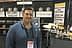 Man standing in front of a booth displaying balsamic vinegar and olive oil products at a trade show. - Olive Oil Times