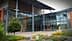 Entrance of a modern building featuring large glass windows and a metal roof structure. - Olive Oil Times
